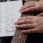 mains sur manche de guitare et tablature imprimee