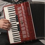 musicien assis jouant un accordéon diatonique rouge